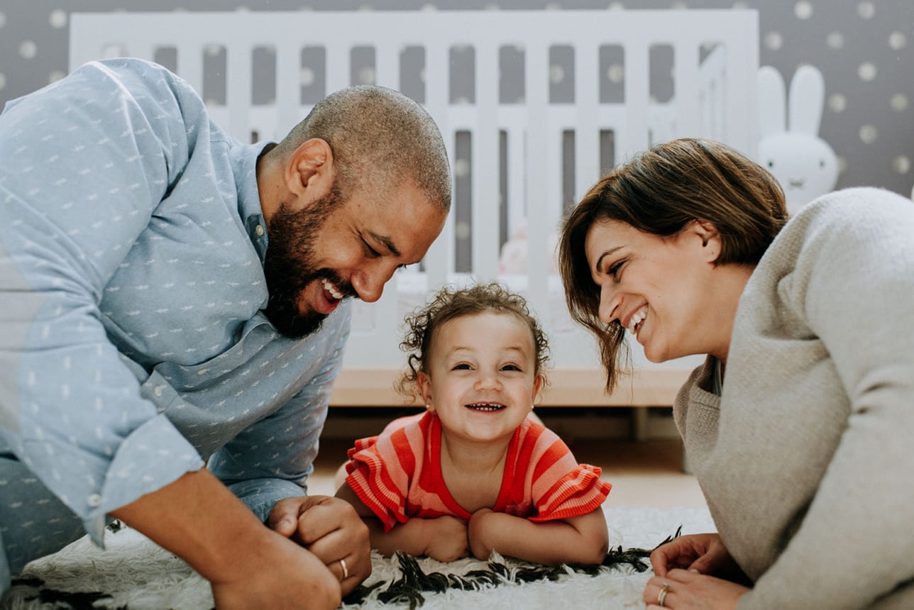 mom and dad hang out with their toddler daughter in her bedroom, laying on the floor and giggling together for Kristyn Miller Photography