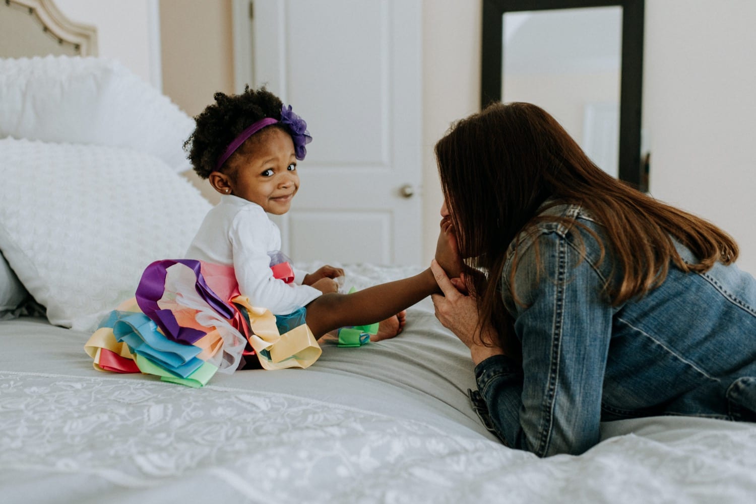 white mom kisses her adopted black daughter's toes while little girl makes a funny face at the camera during this family session at home with Kristyn Miller
