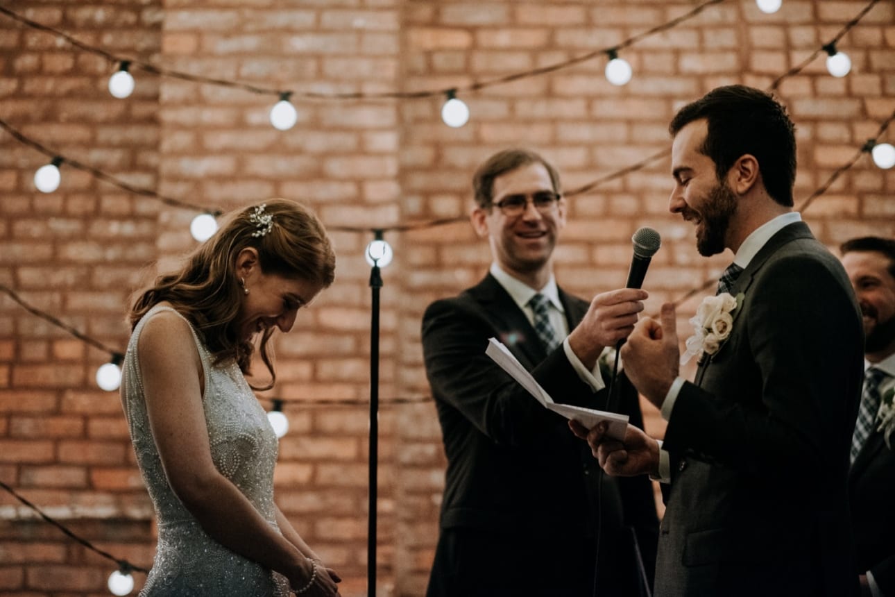 groom makes his bride blush and look down while reading his vows during this mid-winter New York City wedding at 26 Bridge