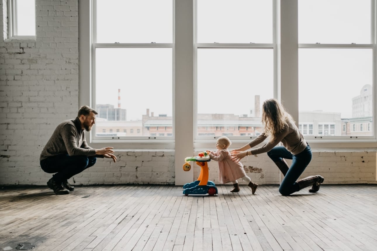 mom helps her baby walk towards dad with the help of a walking toy during this studio family session with Kristyn Miller Photography