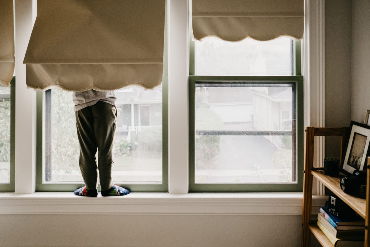little boy stands on a window sill hidden from the waist up by a blind so all you can see is the back of his legs and feet. A blog about Riding The Lion by Kristyn Miller Photography