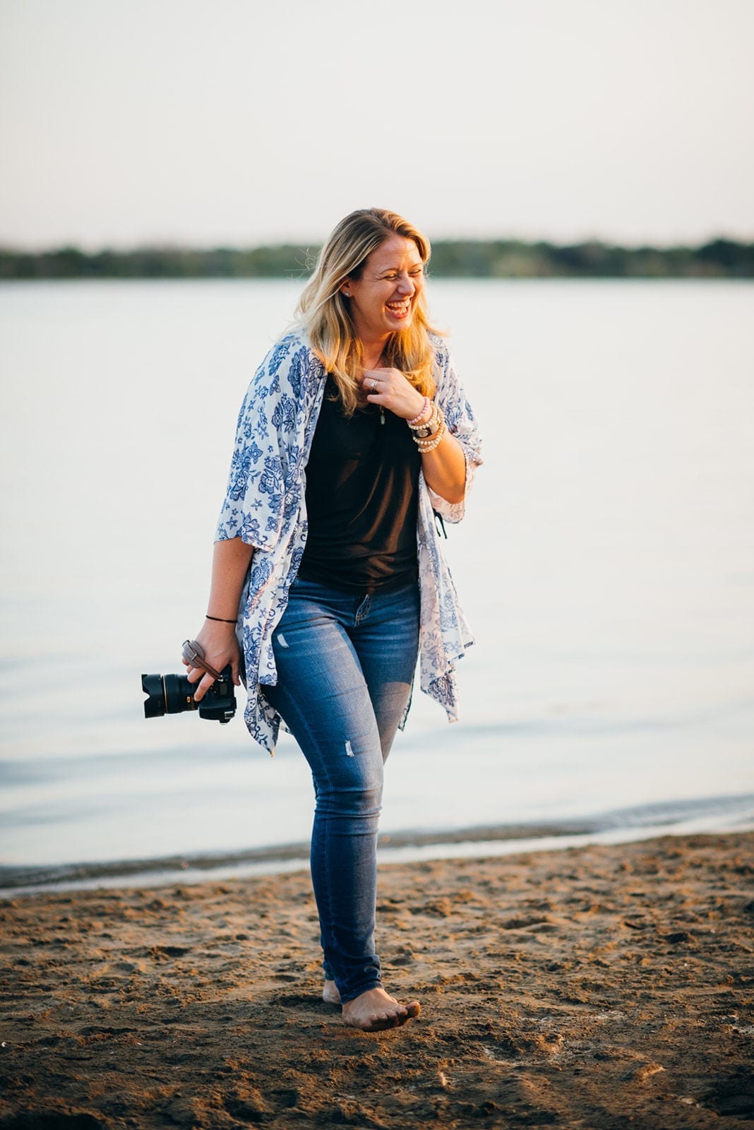 photographer kristyn miller laughs as she walks barefoot on the beach with her camera