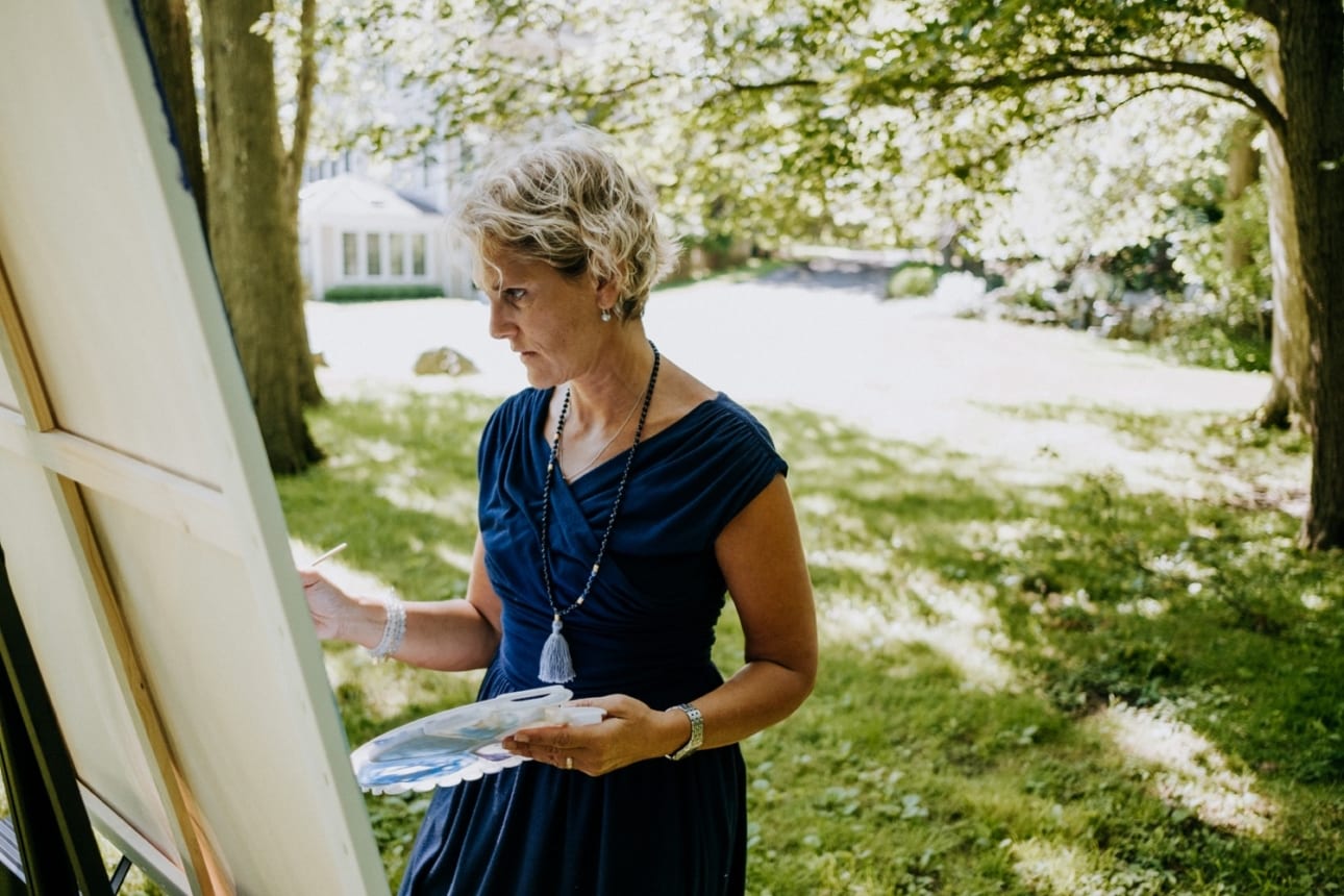 blonde, middle-aged woman paints on a large canvas outside in her backyard showing women in portraits series by Kristyn Miller Photography